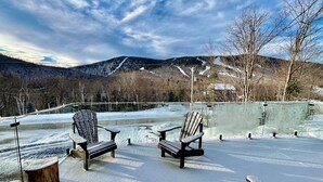 A snow-covered outdoor seating area with Adirondack chairs and benches, overlooking a mountainous landscape.