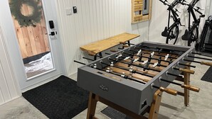A foosball table in a room with a wooden bench, bicycles, and a door leading outside.