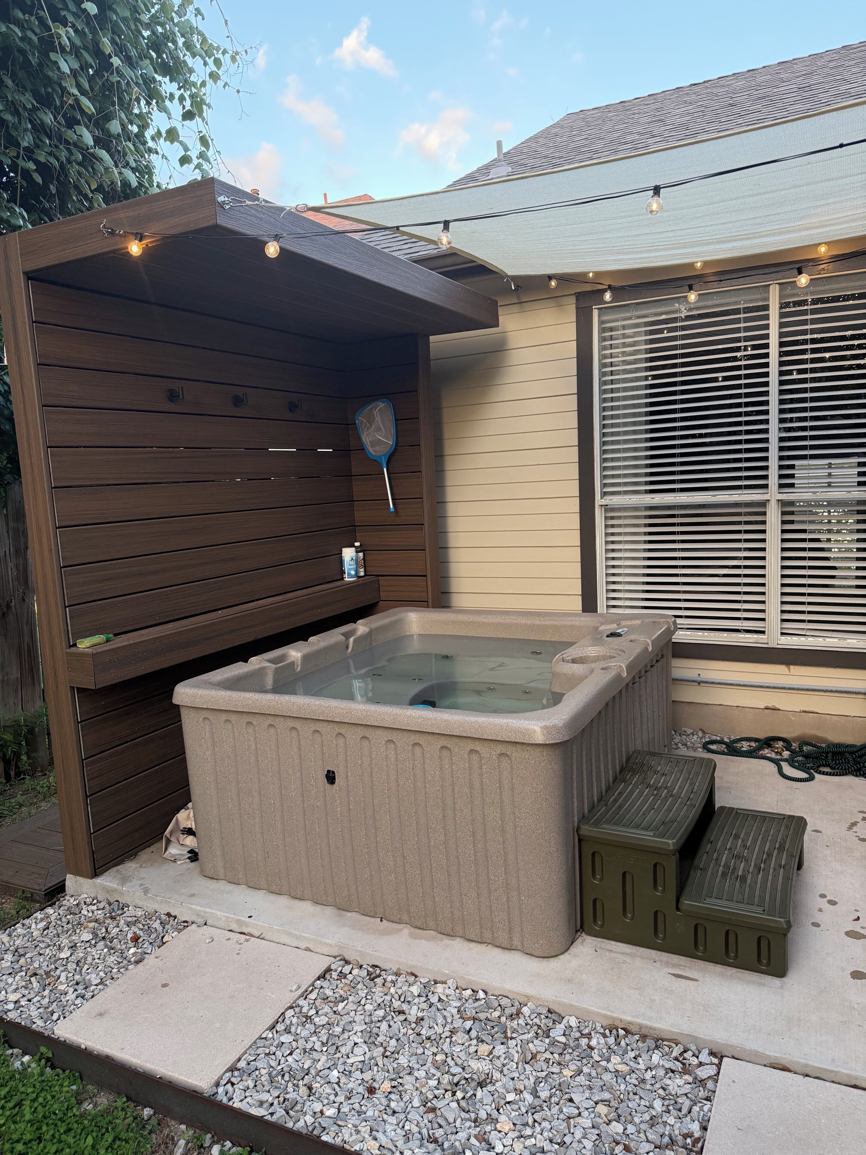 A hot tub with steps, a wooden pergola, and a string of lights.