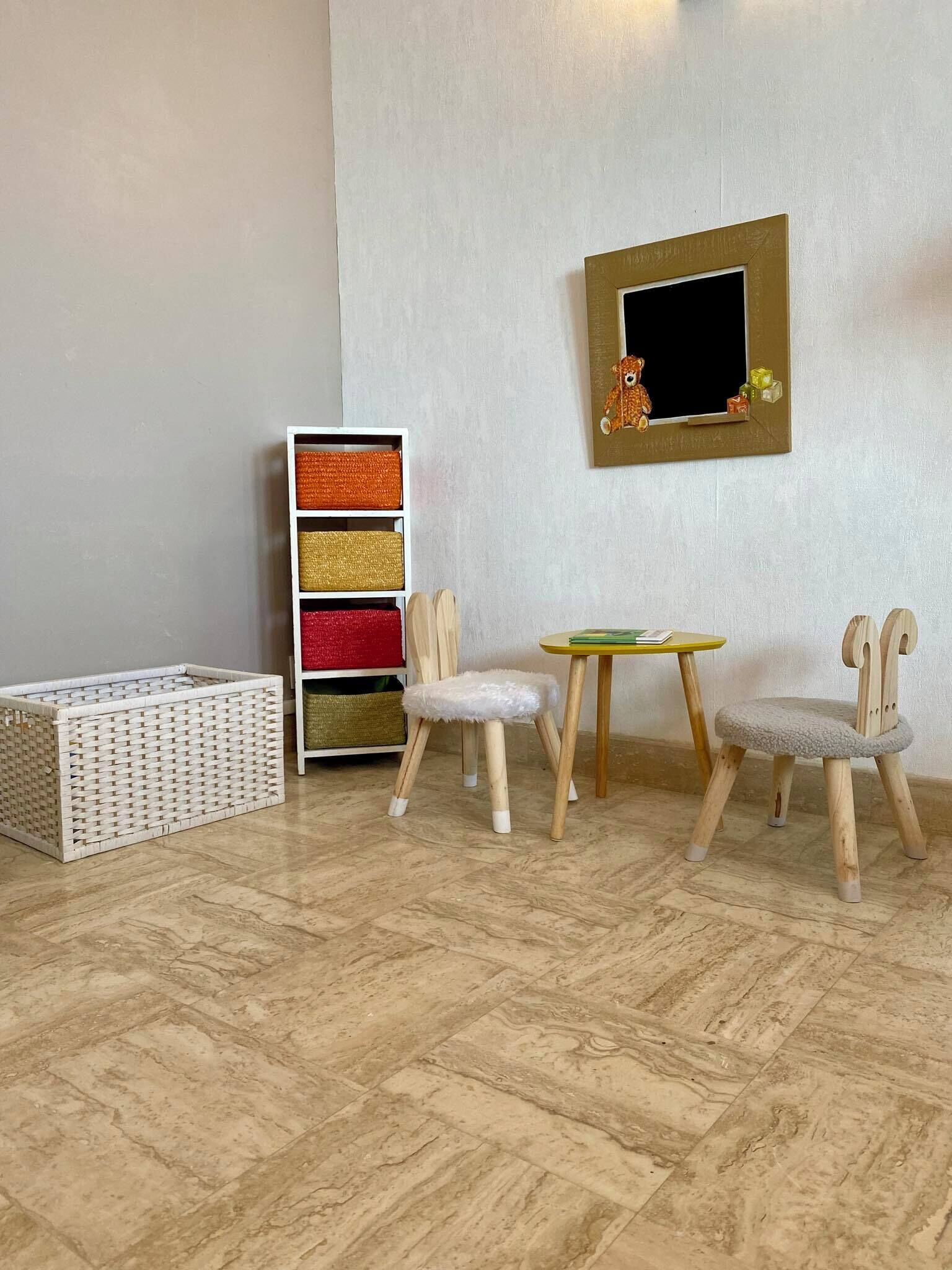 Une pièce dotée d’un parquet en chevrons, d’un meuble de rangement blanc agrémenté de paniers colorés, de deux chaises en bois avec des sièges rembourrés et d’une petite table ronde.