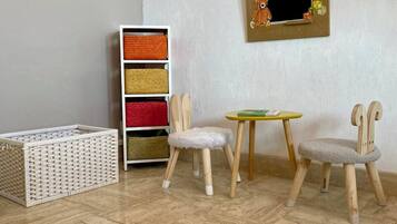Une pièce dotée d’un parquet en chevrons, d’un meuble de rangement blanc agrémenté de paniers colorés, de deux chaises en bois avec des sièges rembourrés et d’une petite table ronde.