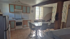 Une cuisine compacte équipée d’une cuisinière, d’un four et d’un réfrigérateur, un coin repas avec une table et des chaises, et un espace de vie avec un canapé.