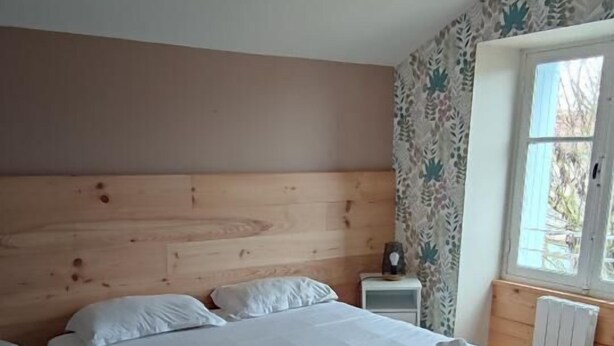 Une chambre à coucher avec une tête de lit en bois, un grand lit avec une literie blanche, deux tables de chevet et une fenêtre donnant sur un beau paysage.