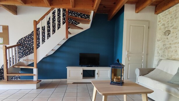 Een woonkamer met een trap, een televisie op een kast, een tafel en een bank.