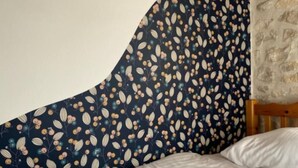Een netjes opgemaakt bed met witte lakens en een opgerolde witte handdoek, een donkerblauwe kaptondeel met bloemenprint, en een wand met een steenstructuur.