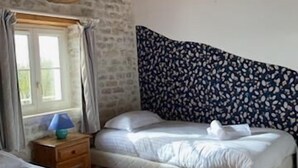 Een slaapkamer met twee bedden, houten balken in het plafond, een behang met patroon en een raam met gordijnen.