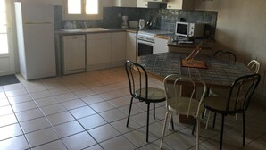 A kitchen with white cabinets, a tiled backsplash, a stove, a microwave, and a dining table with four chairs. - House 14 sleeps 5 2 bathrooms (Ternant)
