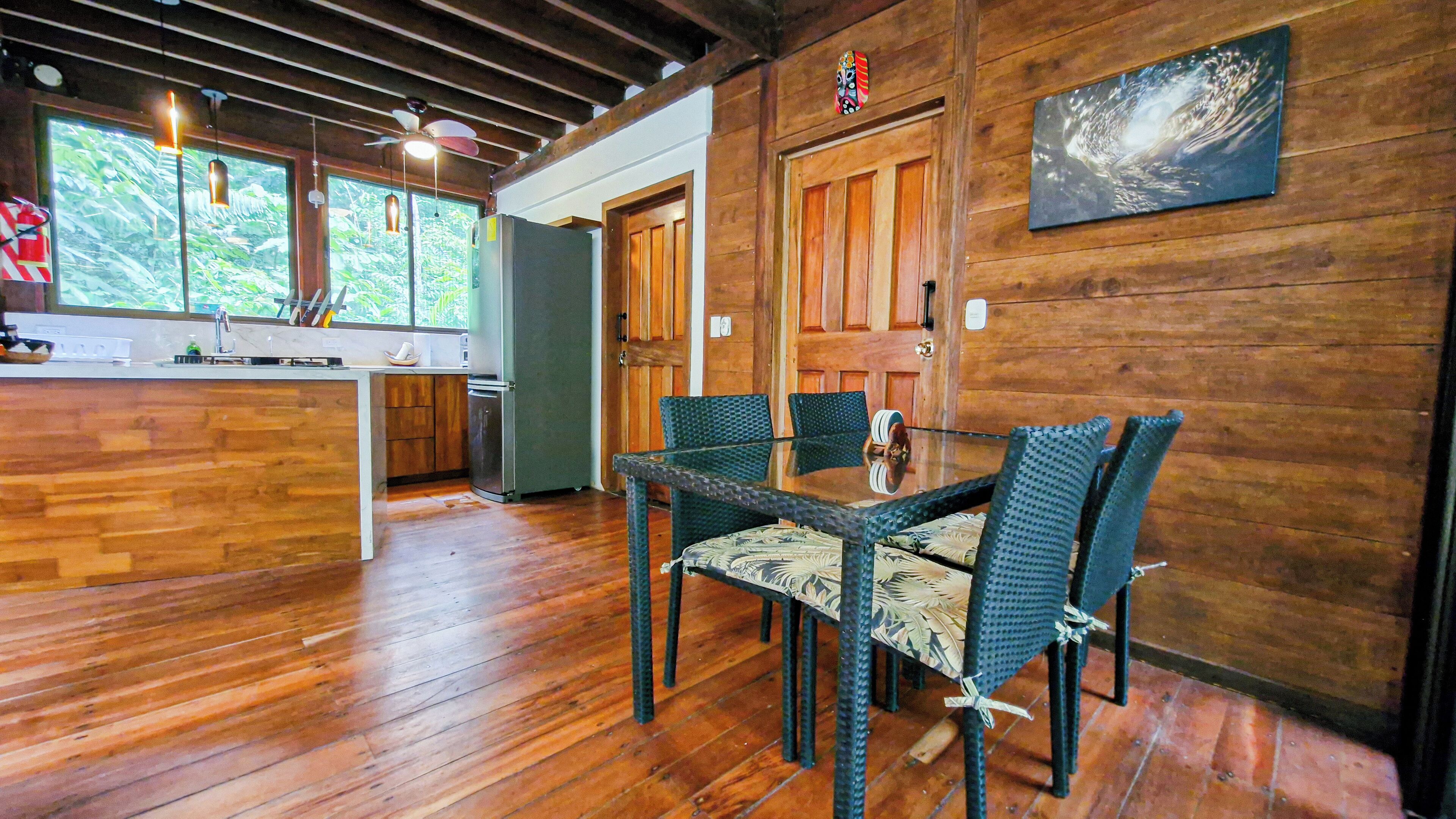 A wooden interior with a kitchen area, a dining table with chairs, and a wooden door.
