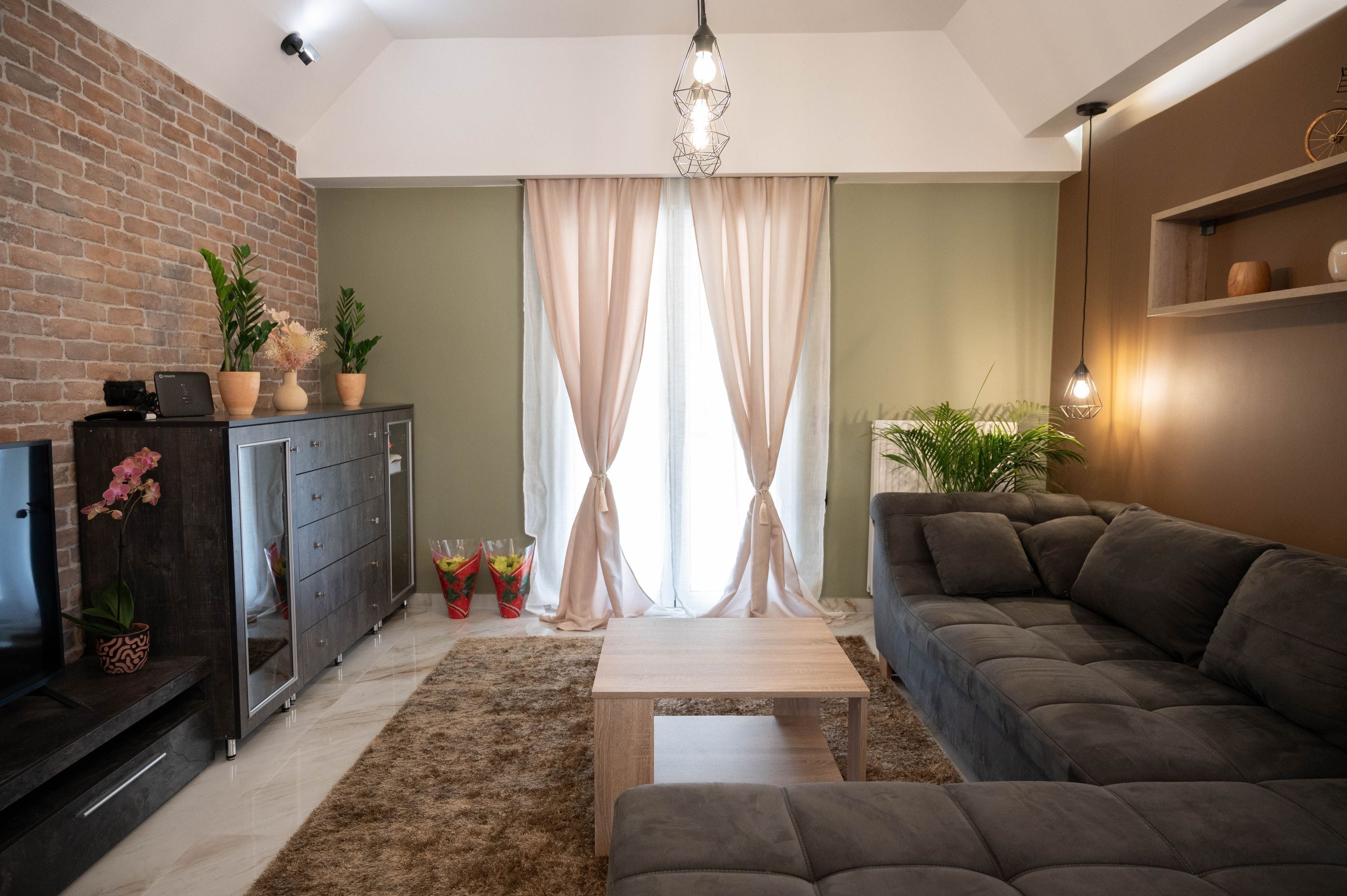 A modern living room with a brick wall, a dark wooden cabinet, a grey sofa, a light wooden coffee table, and a large window with sheer curtains.