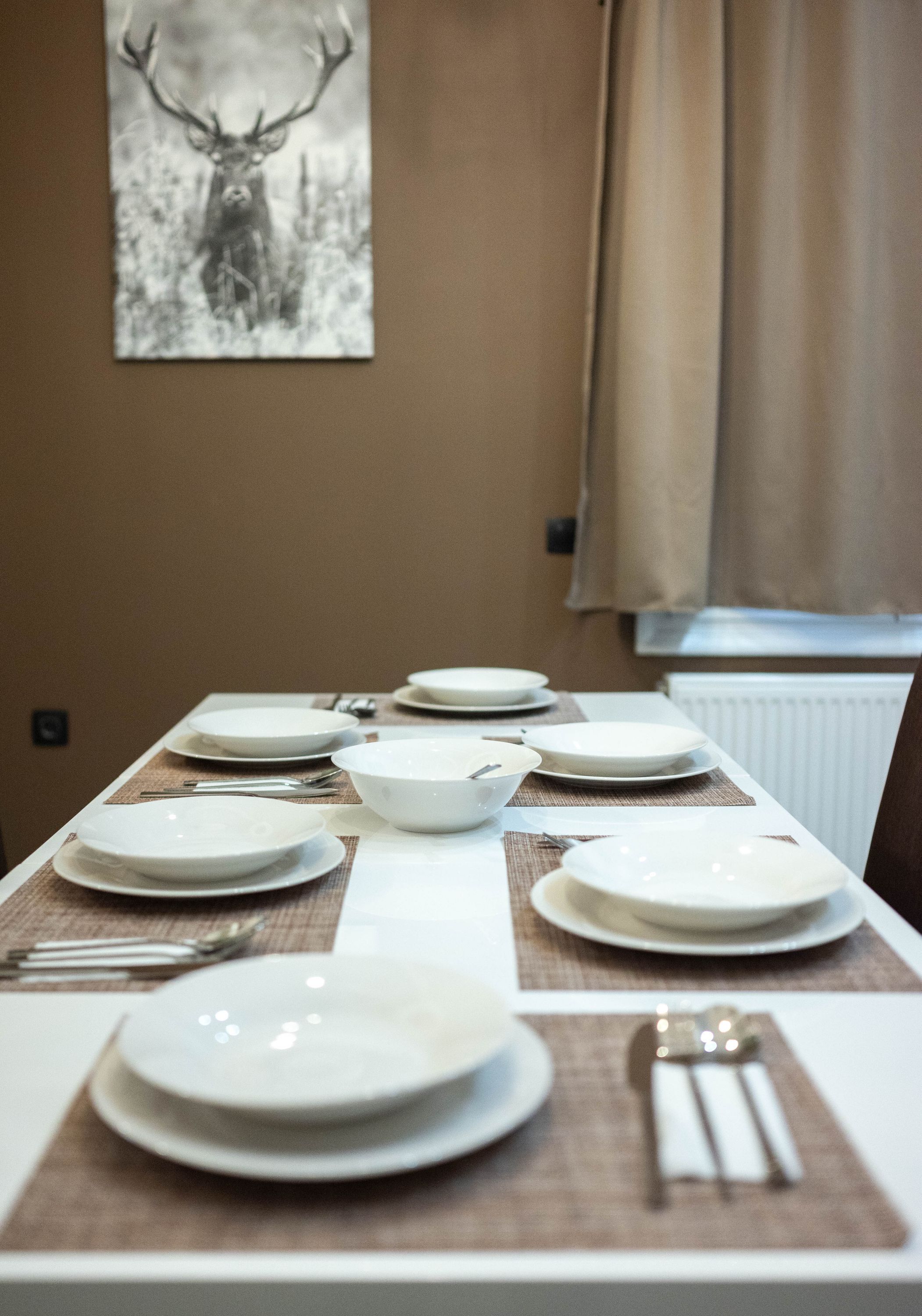 Una mesa de comedor dispuesta con platos, tazones y cubiertos, con un cuadro de un ciervo en la pared de fondo.