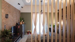 A living room with a brick wall, a sofa, a TV, and a wooden partition. - Aurora Breeze Trikala Town (Trikala)