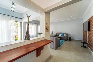 A modern living room with a sofa, a coffee table, and a TV mounted on a brick wall. - Perfect holiday home in Victoria Falls!! (Victoria Falls)