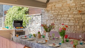 An outdoor dining area with a stone wall, a grill, and various table settings including plates, glasses, and floral centerpieces. - Villa Jadreska by Villas Guide (Kanfanar)