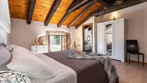 A bedroom with a wooden ceiling, a bed with a patterned blanket, a dresser, and a wardrobe. - Villa Jadreska by Villas Guide (Kanfanar)