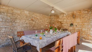 A stone-walled dining area with a table set for four, chairs, a ceiling fan, and a small shelf with potted plants. - Villa Jadreska by Villas Guide (Kanfanar)