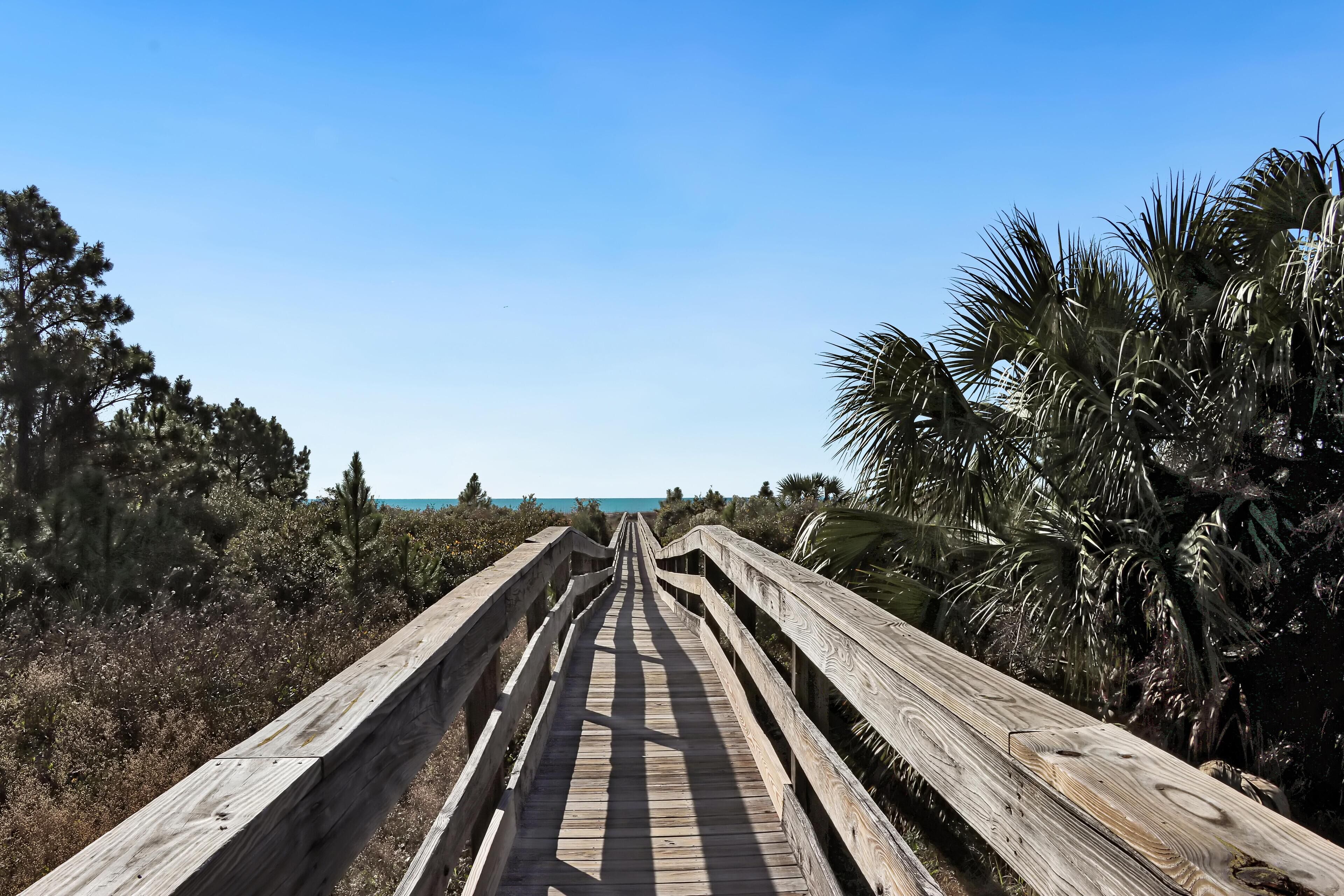 A wooden boardwalk leading to a beach with palm trees and shrubs.