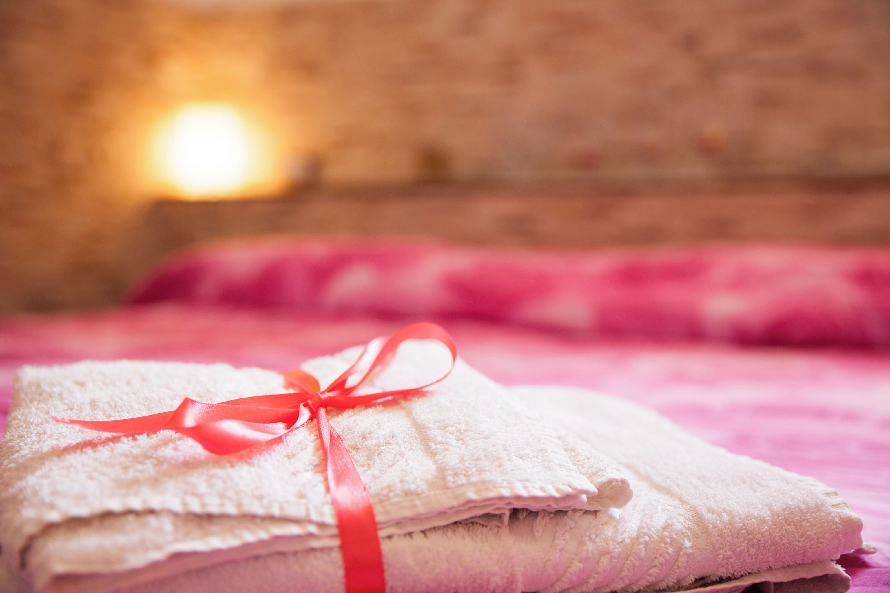 A stack of white towels tied with a red ribbon on a bed with pink bedding.