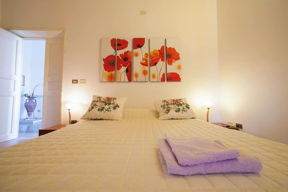 Une chambre d’hôtel avec un grand lit, deux lampes de chevet et un tableau représentant des fleurs rouges au mur.