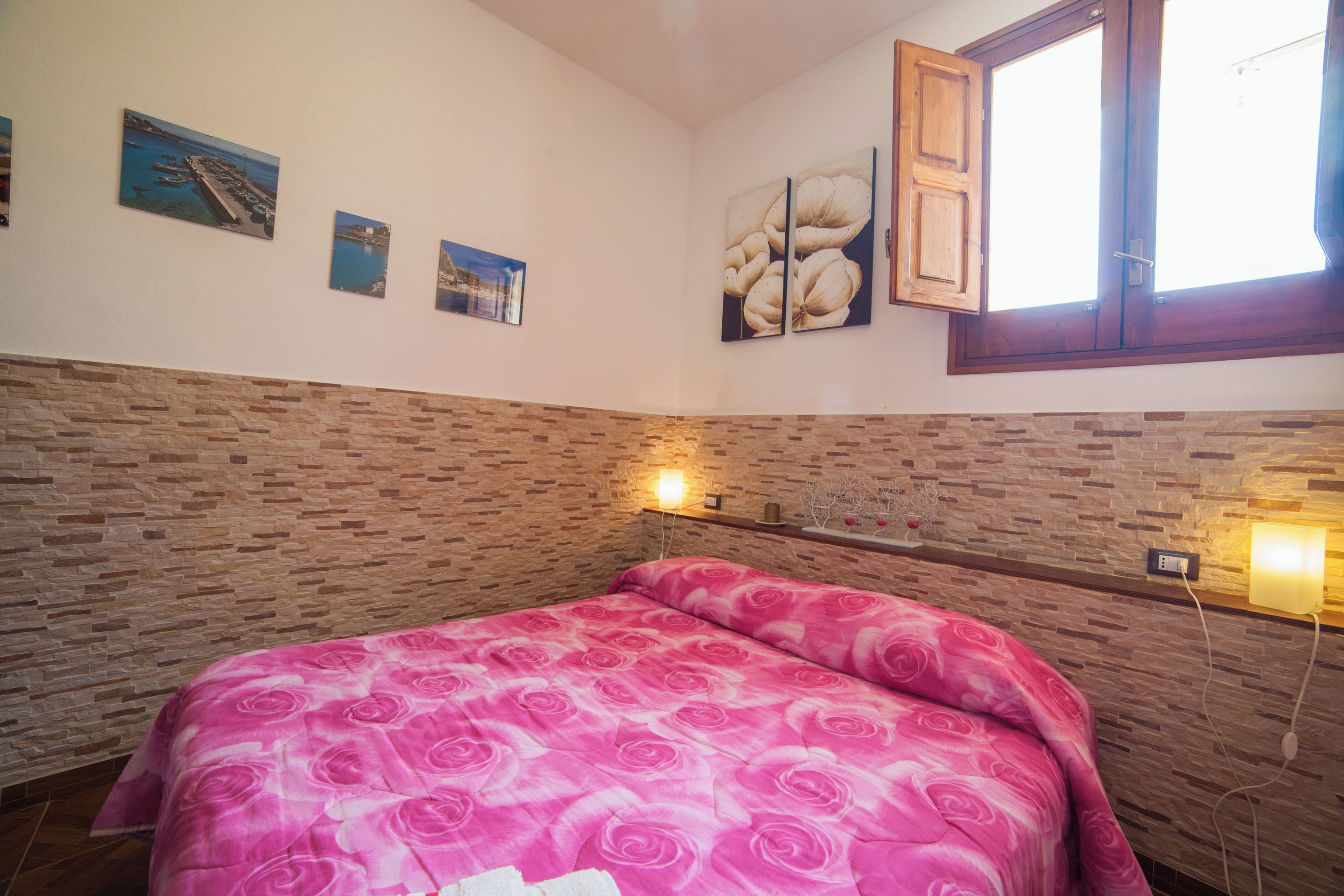 A bedroom with a brick-patterned headboard, a pink floral bedspread, and wall-mounted lights.