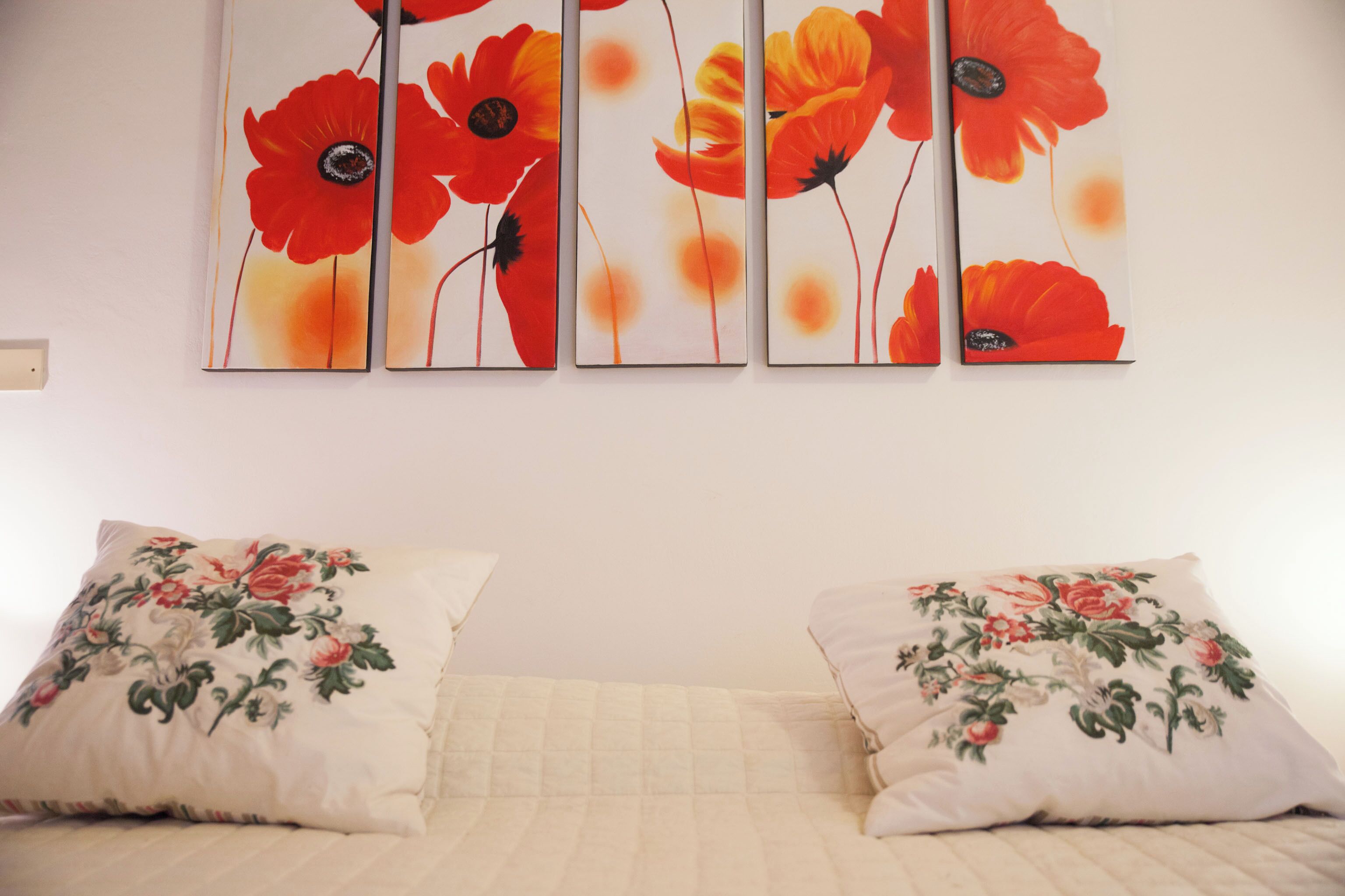A bedroom with a bed, two pillows with floral designs, and a wall-mounted poppy flower painting.