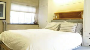 Una cama bien hecha con ropa blanca y almohadas a rayas, un cabecero de madera y una ventana con persianas.
