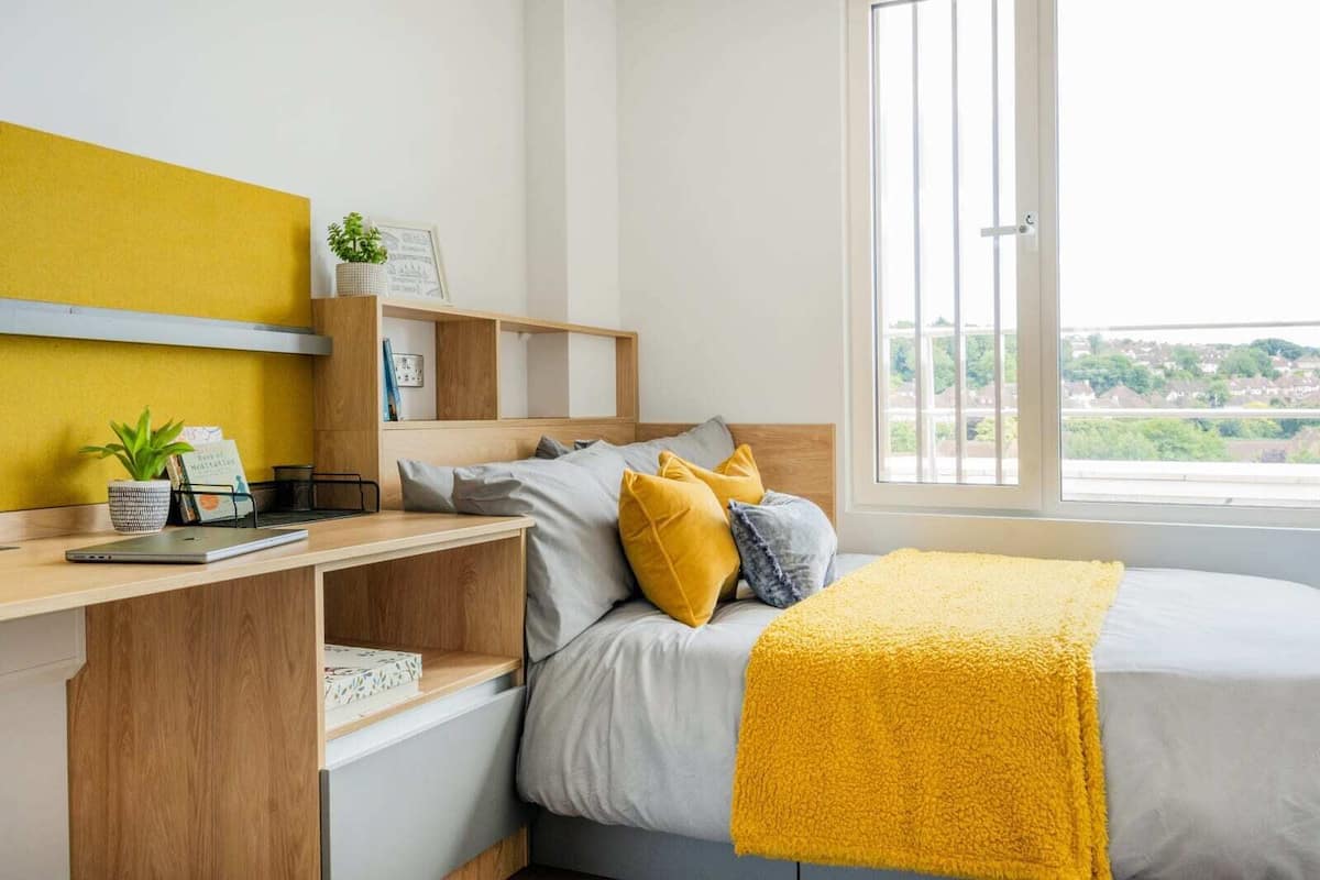 A bedroom with a bed, a desk, and a window.