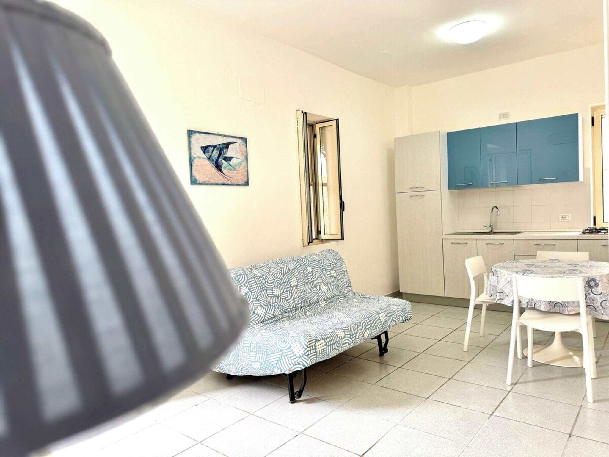 Un salón pequeño y acogedor con un sofá y una mesa de comedor, una cocina con armarios azules, y una obra de arte enmarcada en la pared.