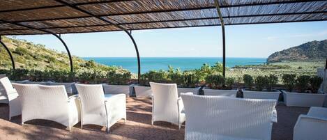 A covered outdoor seating area with white wicker furniture and a view of the sea.
