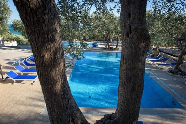 A swimming pool with blue water, surrounded by lounge chairs and trees.