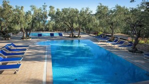 Ein Swimmingpool mit blauen Liegestühlen und Bäumen darum.