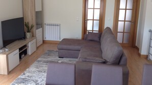Una sala de estar con un sofá seccional, un televisor de pantalla plana, un radiador y dos puertas con paneles de vidrio esmerilado.