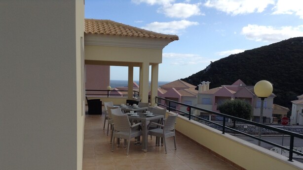 Una terraza con mesa y sillas, un área de estar cubierta y vistas a casas y colinas.