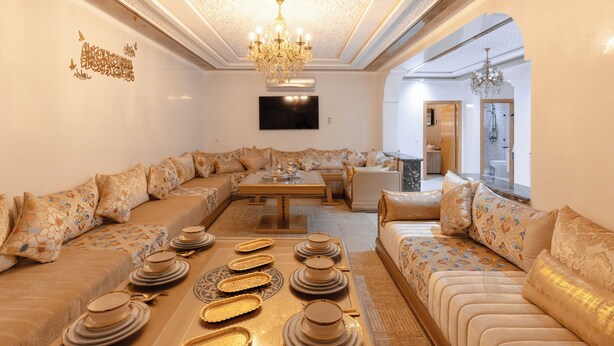 A spacious living room with a large sofa set, a coffee table with dinnerware, and a chandelier. - Appart Hotel Golden Sky Home (Beni Mellal)