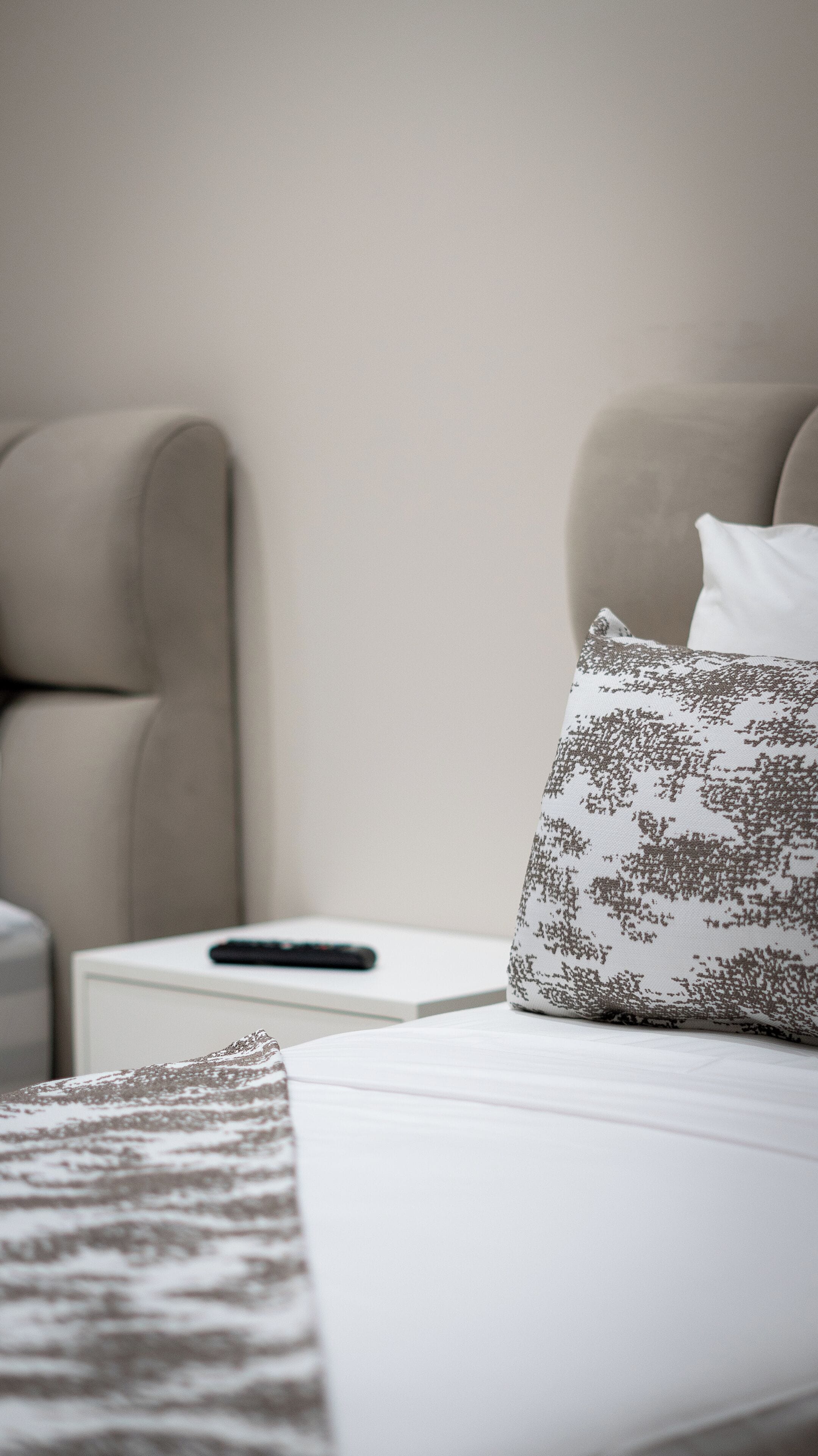 A neatly made bed with a patterned pillow and a remote control on a bedside table.