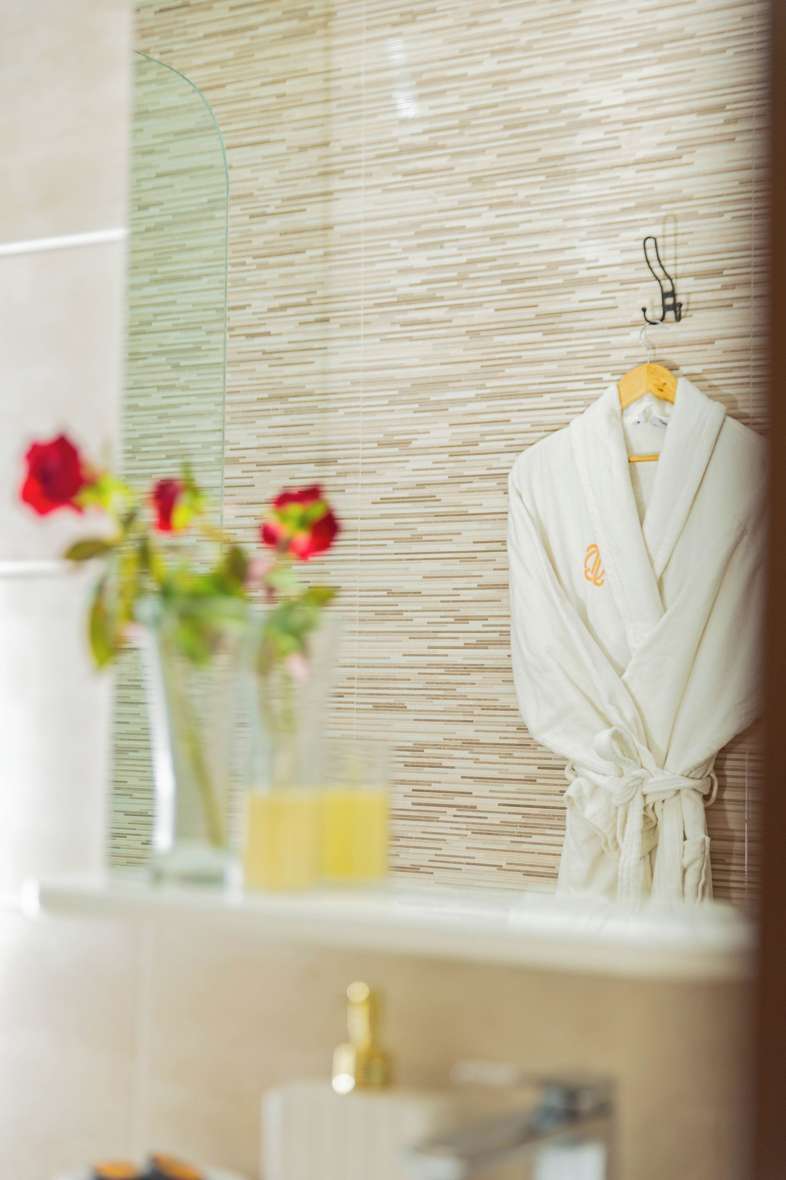 Un baño con toallero, espejo y un florero con flores.