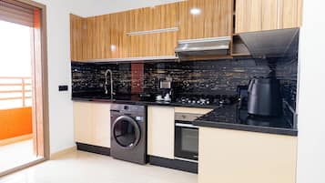 A modern kitchen with wooden cabinets, a washing machine, an oven, and a coffee maker.