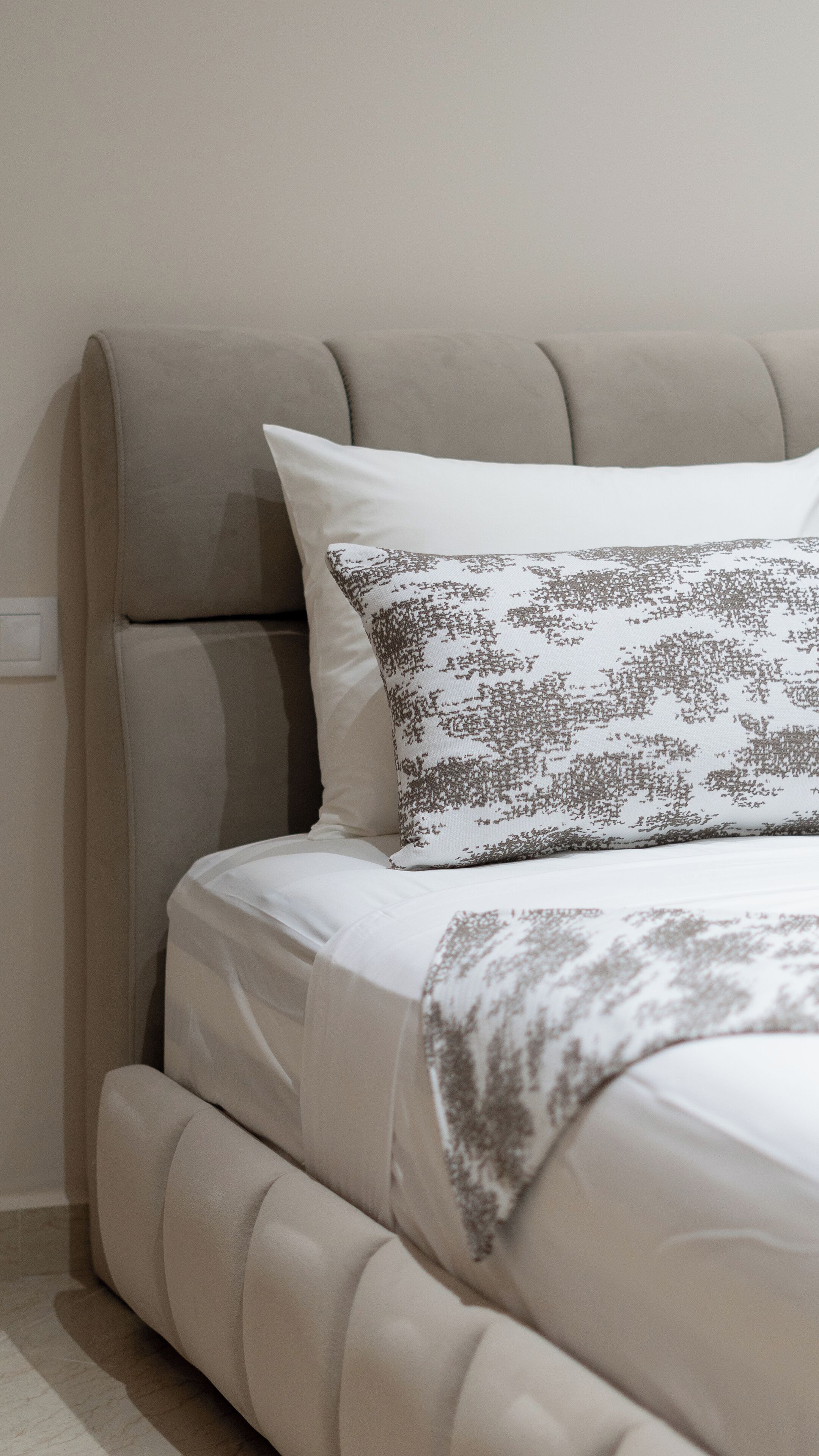 A bed with a headboard, a pillow with a leaf pattern, and a white blanket.