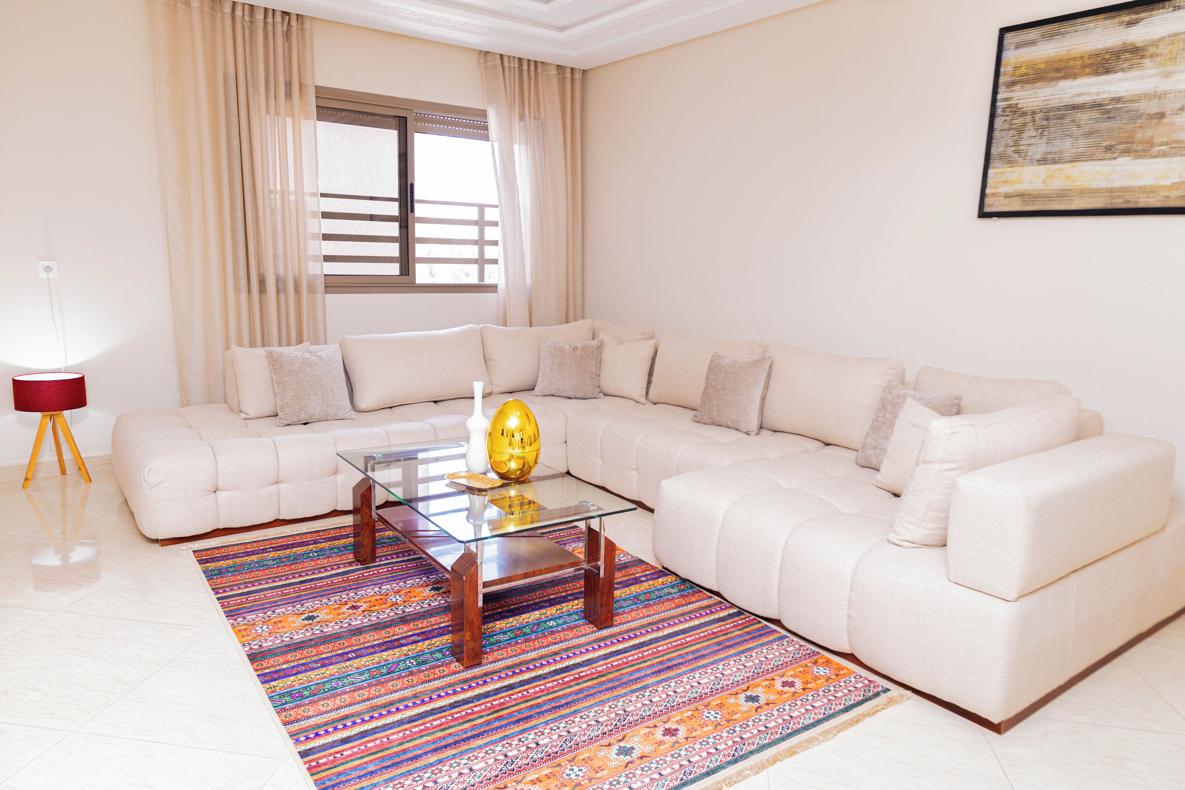 A modern living room with a sectional sofa, a glass coffee table, and a colorful rug.