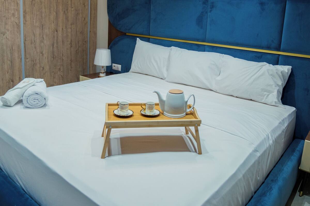 Une chambre d’hôtel avec un grand lit, une armoire en bois, une table de chevet avec une lampe et un plateau avec une théière et des tasses.