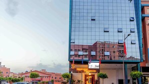 A modern building with a reflective glass facade, a prominent sign for 'Golden Sky Apartment Hotel Cafe & Restaurant', and a flag display at the entrance. - Appart Hotel Golden Sky Home (Beni Mellal)