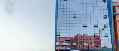 A modern building with a reflective glass facade, a prominent sign for 'Golden Sky Apartment Hotel Cafe & Restaurant', and a flag display at the entrance.