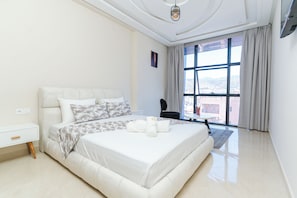 A modern hotel room with a large bed, a small table, a chair, and a large window offering a city view. - Appart Hotel Golden Sky Home (Beni Mellal)