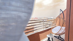 Een balkon met een hangstoel, een tafeltje met een kaars en uitzicht op een stadsgezicht.