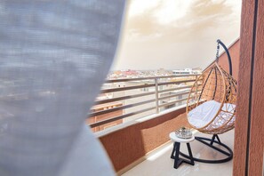 A balcony with a hanging chair, a small table with a candle, and a view of a cityscape. - Appart Hotel Golden Sky Home (Beni Mellal)