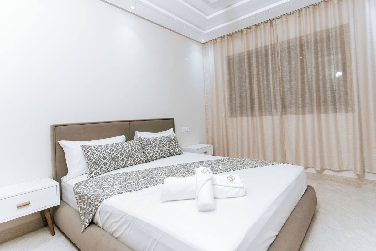 Une chambre d’hôtel avec un lit, des tables de chevet, une fenêtre avec des rideaux et une serviette sur le lit.