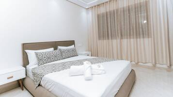 Una habitación de hotel con cama, mesitas de noche, una ventana con cortinas y una toalla sobre la cama.