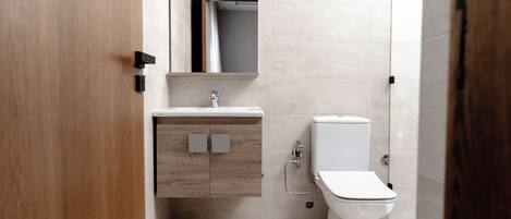 Un baño moderno con tocador de madera, inodoro y zona de ducha.