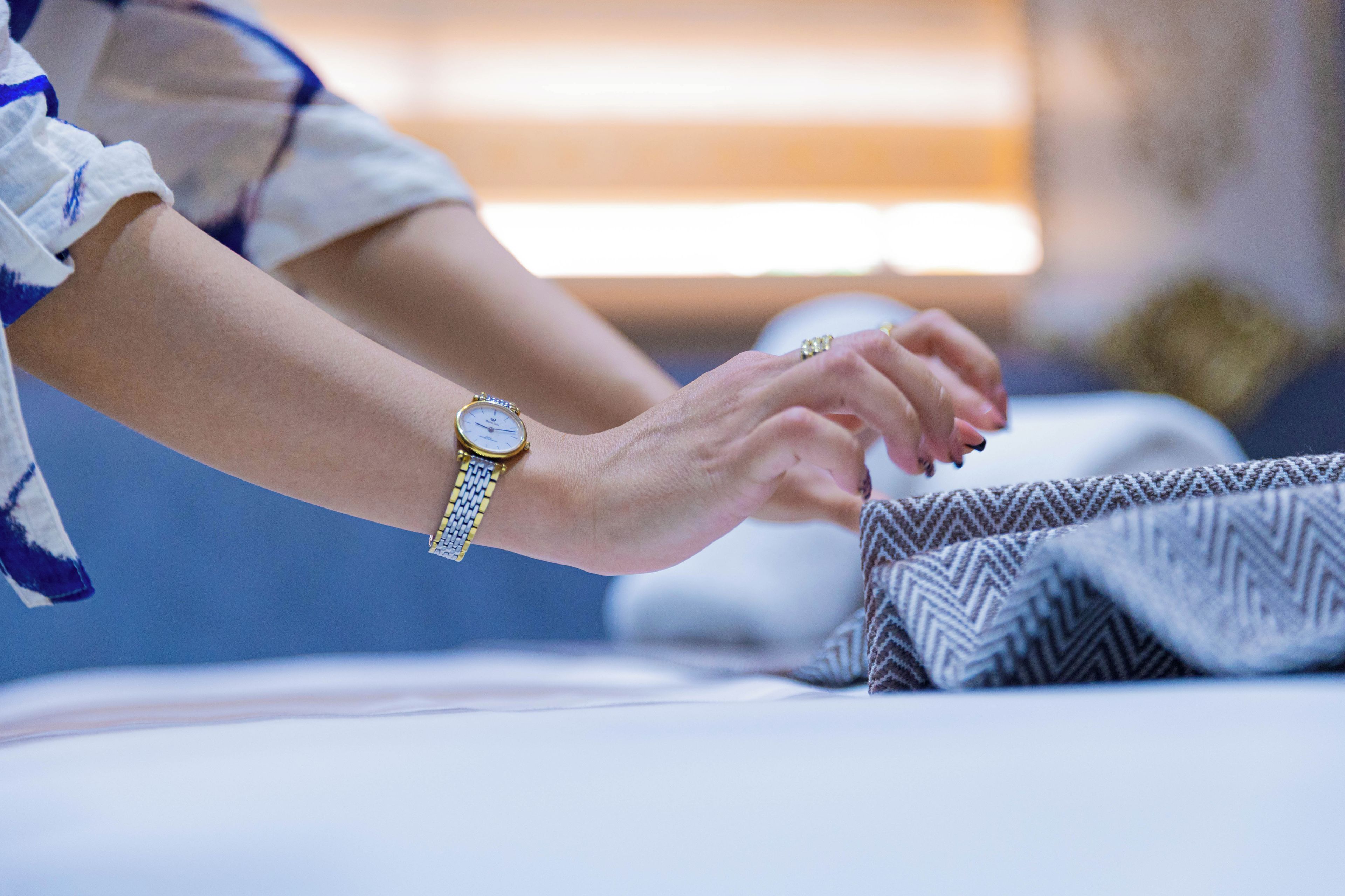A person sitting on a bed with a watch on their wrist.