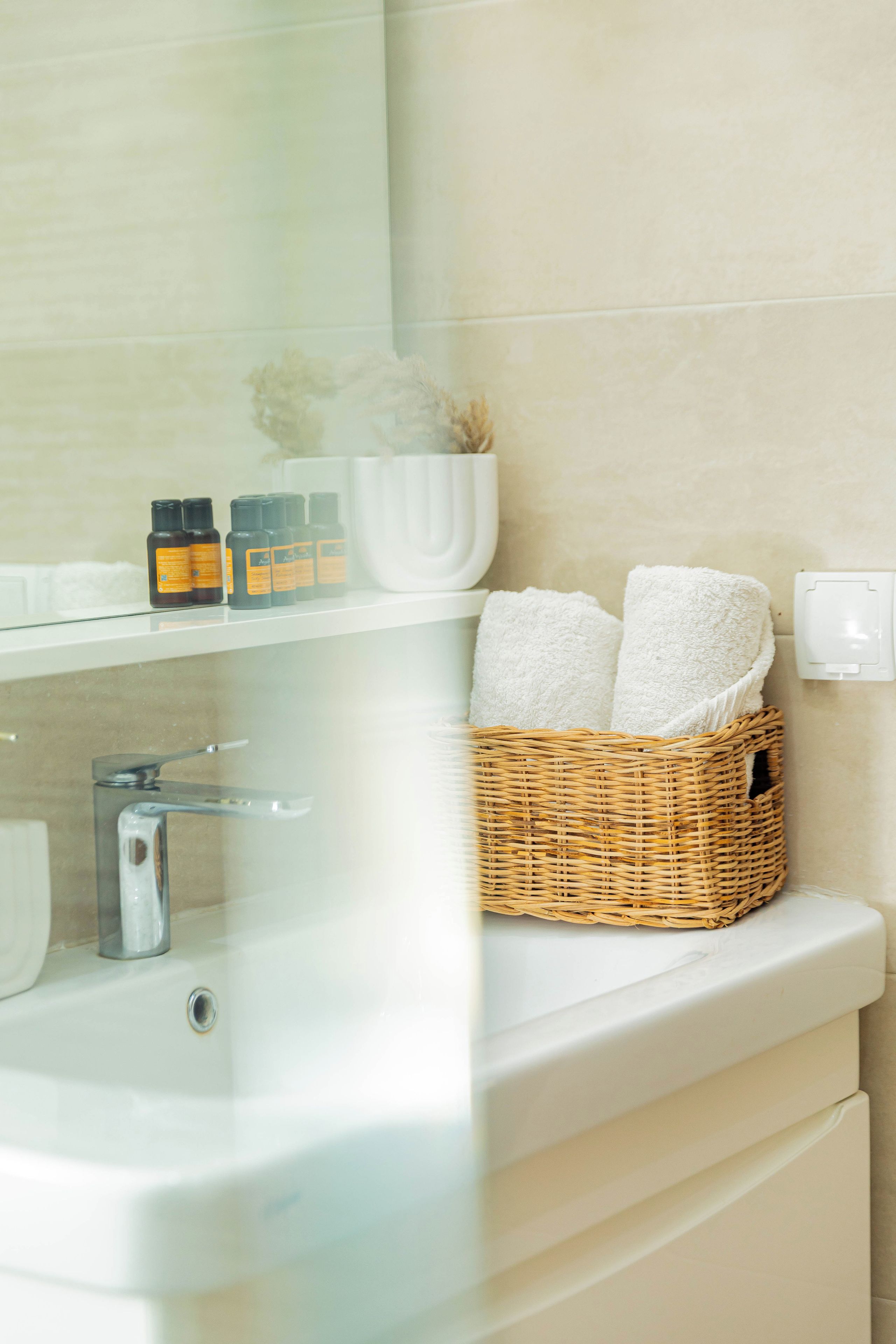 A bathroom with a white sink, a mirror, a white towel holder, and a wicker basket with towels.