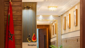 A reception area with a red carpet, a Moroccan flag, a reception desk, and a staircase leading to another floor. - Appart Hotel Golden Sky Home (Beni Mellal)